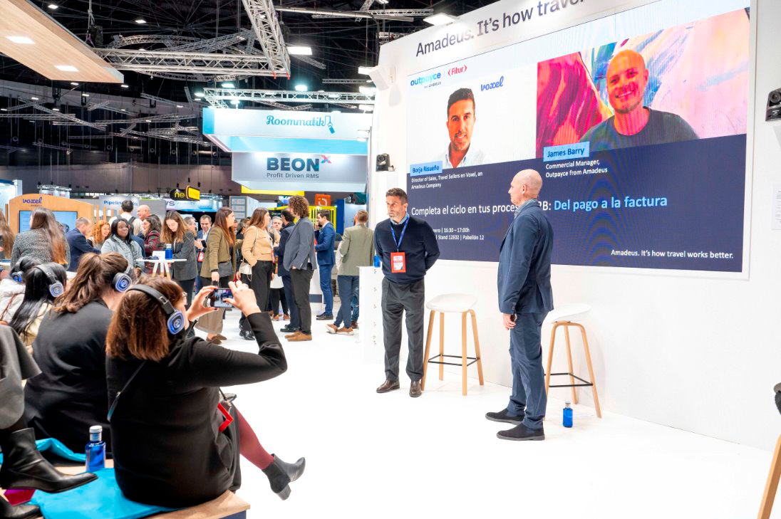 Público con auriculares siguiendo una ponencia en el Ágora del stand de un líder global en travel tech en FITUR 2026